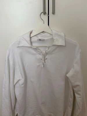 Vit långärmad tröja med snörning - Säljer en vit långärmad tröja med snörning vid halsen och bred krage. Tröjan har en avslappnad passform och är tillverkad i mjukt material, perfekt för en clean och stilren look.