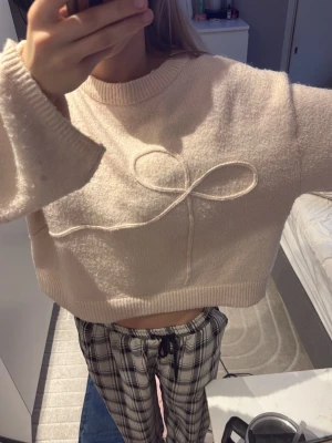 Ljusrosa stickad tröja med rosett - Supersöt ljusrosa stickad tröja med breda ärmar och en dekorativ rosett framtill. Tröjan har croppad passform, ribbade muddar och är gjord i ett mjukt, fluffigt material. Perfekt för dig som gillar en gullig och avslappnad stil.