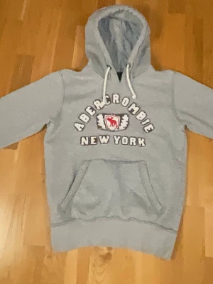 Abercrcombie & fitch  - Snygg grå hoodie från Abercrombie med stor magficka och vit dragsko i huvan. som är storlek S men passar som XS