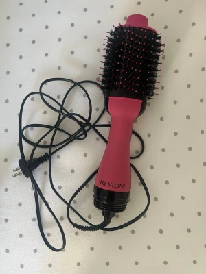 Revlon rosa varmluftsborste - En rosa och svart varmluftsborste från Revlon med ovala borsthuvud och svarta borst med rosa toppar. Perfekt för att styla och torka håret samtidigt. Har sladd med vanlig stickkontakt.