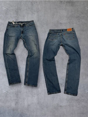 Levi's blå raka jeans - Klassiska blå jeans från Levi's med rak passform och fem fickor. Jeansen har en vintage tvätt och tydliga sömmar. Tillverkade i slitstark denim med knappgylf och läderpatch bak i midjan.