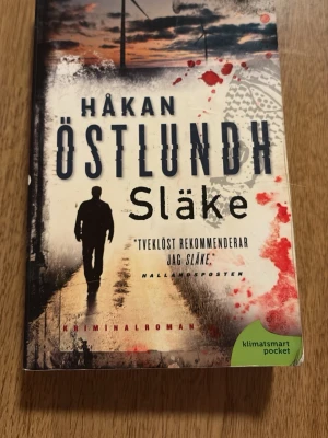 Släke av Håkan Östlundh pocket - Kriminalroman i pocketformat av Håkan Östlundh med titeln Släke. Omslaget har mörka och röda toner med en siluett av en person och blodstänk, vilket ger en spännande och dramatisk känsla. Boken är i pocketformat. Det är första boken i serien av Östlundh