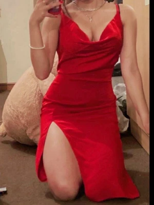 Röd klänning med slits (NWT) - Snygg röd långklänning med smala axelband och djup urringning. Klänningen har en hög slits på ena sidan och figurnära passform. Perfekt för dig som vill sticka ut med en elegant och trendig look.