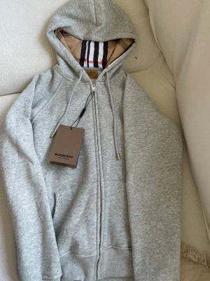 Grå zip hoodie från Burberry - Säljer den för att den inte passar det står att det är en m men passar inte mig som har m då den är för liten så passar perfekt på S och den är helt ny oanvänd 