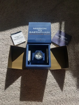 Omega X Swatch Mission to Earthphase klocka - Säljer en Omega X Swatch Mission to Earthphase Moonshine Gold Snoopy från Bioceramic MoonSwatch-kollektionen. Klockan har en blå boett och blått armband, med vit urtavla och detaljer i svart och blått. Kommer i originalbox med tillhörande manualer och certifikat.