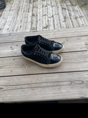 Svarta Lanvin sneakers i läder - Stilrena svarta sneakers från Lanvin i blankt läder med vita sulor och svarta skosnören. Klassisk låg modell med metallöljetter och diskret design. Kommer med originalkartong och dustbags. Köps varan innan 18:00 kommer jag försöka skicka den samma dag beroende på hur det ser ut i schemat mitt. Mycket kvar att ge i skorna. Det är mina bilder bara att jag tog de från min vinted profil.