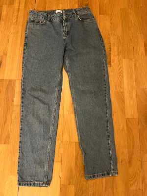 Blå raka jeans i klassisk modell - Ett par blå jeans med rak passform och hög midja. Jeansen har fem fickor, bälteshällor och stängs med dragkedja och knapp. Med stl 164