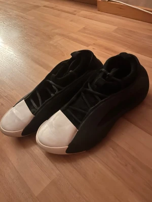 Harden 8 - Snygga sneakers från Adidas i svart mocka med vit tå och sula. Skorna har högt skaft och klassisk snörning. Yttersulan har detaljer i svart, vitt och lila för extra grepp och stil. Perfekta för dig som gillar sportig och clean design.