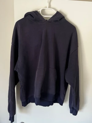 Mörkblå oversized hoodie - En mörkblå oversized hoodie med stor huva och magficka. Hoodien har ribbade muddar vid ärmslut och nederkant. Tillverkad i mjukt bomullsmaterial, perfekt för en avslappnad och chill stil.