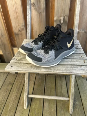 Svarta och grå Nike sneakers Nike air versitile 3 - Snygga sneakers från Nike i svart och grått med vit sula och klassisk Nike-logga i vitt på sidan. Ovandelen är i mesh och syntetmaterial för bra andningsförmåga och komfort. Skorna har svarta snören och en sportig design som passar perfekt till streetwear.