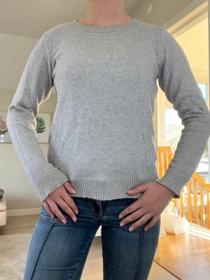 Ljusgrå basic stickad tröja - En enkel och stilren ljusgrå stickad tröja från vila perfekt nu till våren! Grå stickad tröja med rund halsringning och ribbade muddar vid ärmslut och nederkant. Storlek M. Perfekt att matcha med jeans eller kjol för en clean look. Tröjan har en mjuk känsla och klassisk passform. Bara använt några gånger!