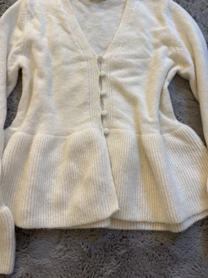 Vit kofta med knappar från Gina Tricot - Mysig vit kofta med v-ringning och dekorativa tygklädda knappar framtill. Koftan har långa ärmar och ribbstickad nederdel som ger en snygg siluett. Perfekt för lager på lager och enkel att matcha med olika outfits. Säljer då den inte kommit till någon användning ☺️endast provad så är som ny i skicket💕💕