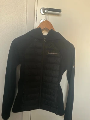 Svart dunjacka Peak Performance - Snygg svart dunjacka/vårjacka från Peak Performance med huva och dragkedja framtill. Jackan har en slimmad passform, quiltade paneler och diskret logga på bröstet. Perfekt för vädret nu. Storleken är S men den känns mer som XS. Ordinarie pris 2400kr.                            Bara skriva om man vill se fler bilder eller hur de sitter på💞