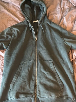 Mörkgrön hoodie med dragkedja - Snygg mörkgrön hoodie från Weekday med dragkedja framtill och stora fickor på magen. Klassisk huva med dragsko och ribbade muddar vid ärmslut och nederkant. Perfekt för en avslappnad och cool stil.