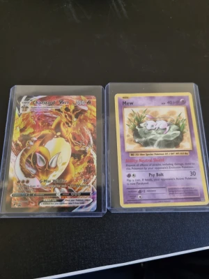 Pokémonkort Charizard VMAX & Mew - Två Pokémonkort i plastfickor: Charizard VMAX med eldig bakgrund och holografisk effekt samt Mew med lila ram och klassisk design. Perfekt för samlare. Skriv vid prisförslag