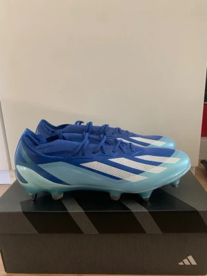 Blå Adidas fotbollsskor med skruvdobbar - Snygga fotbollsskor från Adidas i blått och ljusblått med vita detaljer och klassiska ränder på sidorna. Skorna har snörning och metall-dobbar för bra grepp på planen. Säljer för jag köpte dem i fel storlek. Kan sänka i pris. 