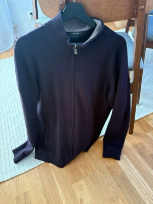 Mörkblå ziptröja Massimo Dutti - Snygg mörkblå ziptröja från Massimo Dutti med hög ribbad krage och dragkedja framtill. Tröjan har ribbade muddar vid ärmslut och nederkant samt två fickor. Perfekt för lager på lager och stilren look.