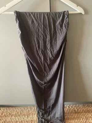 Grå långkjol från Gina Tricot - En svart långkjol från Gina Tricot i stretchigt och mjukt material. Kjolen har en enkel, rak modell utan synliga detaljer eller mönster, vilket gör den lätt att styla med olika toppar och accessoarer.