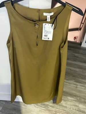 Olivgrön ärmlös klänning H&M - Stilren olivgrön klänning från H&M i ett mjukt, lätt material. Klänningen är ärmlös med rund halsringning och en knappdetalj framtill. Enkel och clean design som passar perfekt till sommaren.