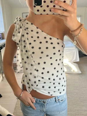 Prickig oneshoulder topp med rosett - Snygg vit oneshoulder topp med svarta prickar från H&M. Knappt använd