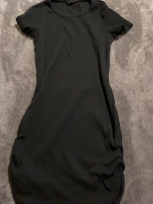 Svart kortärmad klänning - En enkel och stilren svart klänning med korta ärmar och rund hals. Modellen är rak och kort, perfekt för en clean och avslappnad look. Passar dig som gillar minimalistisk stil och vill ha något bekvämt men ändå snyggt.