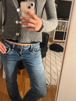 Grå kofta med knappar -  grå kofta från oss Molly med långa ärmar och stora vita knappar framtill. Koftan har en croppad passform och ribbstickade muddar vid ärmslut och nederkant. Perfekt att slänga över en topp