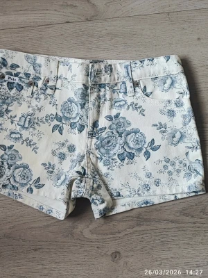 Helt ny shorts från Polo Ralph Lauren - Snygga vita shorts från Polo Ralph Lauren med blått blommigt mönster. Klassisk femficksmodell med bälteshällor och knappgylf. Perfekta för sommaren och ger en fräsch och trendig look. Midjemått: 35 cm,xs