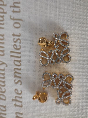 Guldiga örhängen med gnistrande stenar - Unika örhängen i guldfärg med fyrkantig, öppen design och massor av små gnistrande stenar som ger en lyxig känsla. Örhängena har ett elegant mönster och stift med säkerhetslås. Perfekta för dig som vill sticka ut med accessoarerna.