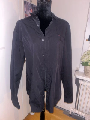 Svart skjorta från Tommy Jeans - Snygg svart skjorta från Tommy Jeans i slim fit-modell. Skjortan har klassisk krage, knappar framtill och en liten logga på bröstet. Tillverkad i mjuk bomull som känns skön mot huden. Perfekt för dig som gillar stilrena och tidlösa plagg.