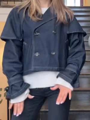Mörkblå cropped jeansjacka - OBS! plagget är liten i storleken : jag har vanligtvis Xs eller S och denna sitter perfekt på mig! Unik mörkblå jeansjacka med dubbelknäppning och bred krage. Jackan har en cropped passform och extra lager över axlarna som ger en cool, trendig look. Perfekt för dig som vill sticka ut med en modern twist på klassisk jeansjacka.