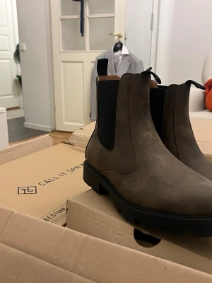 Bruna Chelsea boots från Call It Spring - Säljer ett par snygga bruna Chelsea boots från Call It Spring. Boots i veganskt material med elastiska svarta paneler på sidorna och grov sula. Klassisk siluett med dragflikar fram och bak för enkel påtagning. Perfekta för dig som vill ha stilrena och trendiga boots.