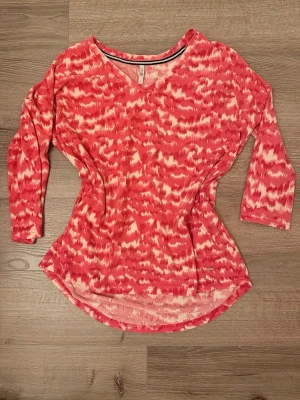 Rosa mjukt mönstrad topp  - Säljer en rosa och vit topp från Hanes med v-ringning och trekvartsärm. Toppen har ett abstrakt mönster och är tillverkad i ett mjukt, stretchigt material som känns skönt mot huden.