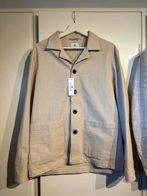 Beige overshirt från John Henric - Stilren beige overshirt från John Henric i ett lätt, luftigt bomullstyg. Perfekt till sommaren! Skick: 9,5/10 oanvänd. Pris 399. Storlek: s. Bara att fråga om det är något!