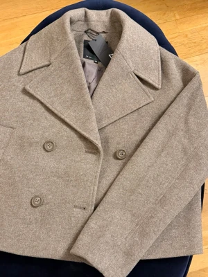 Beige skepparkavaj från Weekday - Stilren skepparkavaj i beige från Weekday med dubbelknäppning och breda slag. Kavajen har en klassisk, rak passform och är tillverkad i ett mjukt ullblandat material. Perfekt för dig som vill ha en tidlös och trendig look.