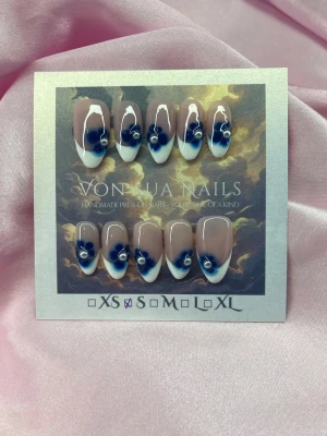 Sthlm (S);Medim Almond - Handgjorda press-on naglar i en medium mandelform med nude bas, vit fransk tipp och blå blommor med vita detaljer. Perfekt för dig som vill ha en unik och kreativ nageldesign. S: 15 mm, 11,5 mm, 12 mm, 11 mm, 9 mm,och designen är elegant och trendig.