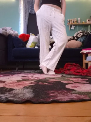 Vita linnebyxor med dragsko - Säljer ett par vita linnebyxor med avslappnad passform och dragsko i midjan. Byxorna har raka ben och resår i midjan för extra komfort. Perfekta för en chill och stilren look. Materialet är lätt och luftigt linne.