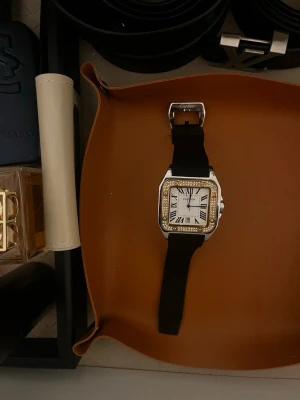 Seiko Santos  - Step into a legacy of aviation-inspired luxury with the Heritage Santos "Iced" Edition. This timepiece reimagines the iconic square silhouette with a modern, high-fashion twist. Featuring a brilliant diamond-encrusted bezel and a striking two-tone gold and silver finish, this watch is designed for those who demand both classic elegance and contemporary "iced out" flair.  Paired with a durable, textured performance strap, it offers a sophisticated architectural presence that transitions seamless