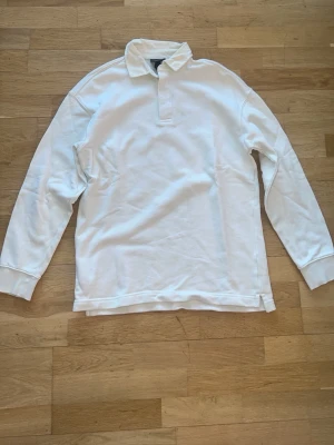 Vit långärmad tröja i bomull - Klassisk vit rugbytröja med lång ärm och krage. Tröjan har ribbade muddar vid ärmsluten och en rak passform. Perfekt för en clean och sportig stil. Materialet känns mjukt och bekvämt, och är i bomull. 