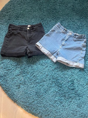 Jeansshorts i svart och ljusblå - Säljer två par jeansshorts, ett par ljusblåa och ett par svarta. Plaggen är i bra skick och är perfekta till sommaren. Midjan är går att justera och benen går att rulla upp så att man kan anpassa längden till sin smak. Shortsen är i storlek 146 💞