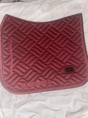 Vinrött schabrak från Equestrian Stockholm - Säljer ett snyggt vinrött schabrak från Equestrian Stockholm i storlek COB. Schabraket är helt nytt och aldrig använt. Nypris: 899 kr