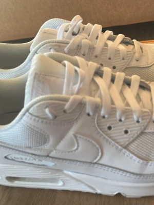 Nike Air Max 90 vita sneakers str 44 - Snygga helvita Nike Air Max 90 sneakers med klassisk siluett. Skorna har ovandel i en mix av läder och mesh för både stil och komfort. Tjock sula med synlig Air-enhet ger extra dämpning och streetkänsla. Perfekta för dig som gillar en clean och sportig look. Använda väldigt få gånger 