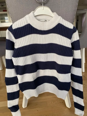 Randig stickad tröja från 157 - Säljer en ribbstickad tröja från 157 med breda marinblå och vita ränder. Tröjan har rund halsringning och långa ärmar. Perfekt för dig som gillar klassisk och avslappnad stil. Köparen står för frakt.