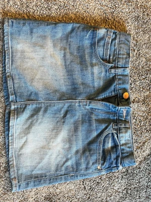 Blå jeanskjol från Gap - Säljer en klassisk blå jeanskjol från Gap med femficksmodell, knapp och dragkedja framtill samt bälteshällor. Kjolen har en kort passform och är tillverkad i slitstarkt denimtyg. Perfekt till sneakers eller boots för en avslappnad look.