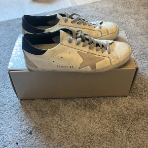 Vita Golden Goose sneakers med stjärna - Säljer ett par vita Golden Goose sneakers för att de inte kommer till användning. Storleken är 40 men passar 41-41,5. Skorna är i helt ok skick mest för att det har blivit hål i hälen på båda skorna  men som har lagats och limmats fast (se bild 4) skorna köptes på Plick för 2000-3000kr  har ej kvitto men säljaren jag köpte av hade digitalt på farfetch och kan bekräfta att de är äkta. Man får med skokartong och bag! Skriv om ni undrar något! MVH Arvid