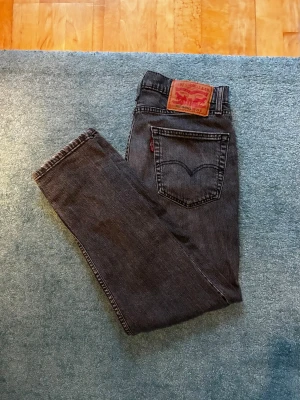 Grå Levi's 502 Hi-Ball - Storlek: W29 L32. Säljer ett par klassiska grå Levi's 502 Hi-ball jeans med slim passform och fem fickor. Jeansen har den ikoniska röda Levi's-lappen på bakfickan och är tillverkade i slitstark denim. Perfekta för en grisch och stilren look.