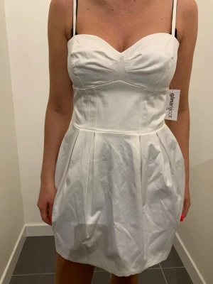 Vit kort klänning från Gina Tricot ny - Snygg vit kort klänning från Gina Tricot med justerbara smala axelband och markerad midja. Klänningen har en söt sweetheart-urringning och lätt utsvängd kjol. Perfekt för sommarens alla tillfällen.