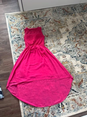 Rosa långklänning med spetsliv - Snygg rosa långklänning med spetsdetaljer upptill och ärmlös design. Kjolen är i ett tunt, svepande material som ger en elegant look. Perfekt för dig som vill sticka ut med färg och stil.