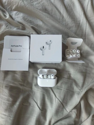 Apple AirPods Pro trådlösa hörlurar - Säljer ett par vita Apple AirPods Pro med laddningsetui och extra silikontoppar. Hörlurarna är trådlösa och har en stilren, kompakt design i plast. Perfekta för dig som vill ha grymt ljud och smidig anslutning till din iPhone eller annan Apple-enhet.