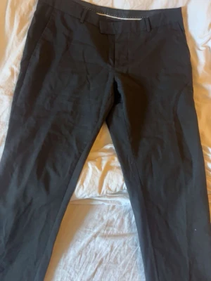 Svarta kostymbyxor från Bläck - Snygga svarta kostymbyxor från Bläck i modellen Tailored Fit. Byxorna har klassisk design med hällor för bälte och diskreta fickor. Perfekta för en stilren look och tillverkade i ett bekvämt material som ger en dressad känsla.