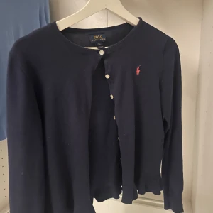 Mörkblå kofta från Polo Ralph Lauren - Säljer min jättesnygga mörkblå tunna kofta från Polo Ralph Lauren då den är lite för liten för mig. Barn storleken är XL men jag skulle säga Dam XS eller XXS. Tröjan har ett litet hål längst ned men det märks knappast och därav priset❤️